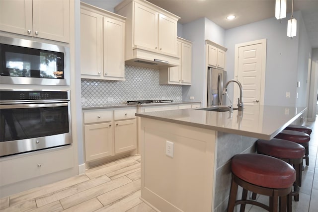 kitchen featuring decorative backsplash, appliances with stainless steel finishes, a sink, under cabinet range hood, and a kitchen bar