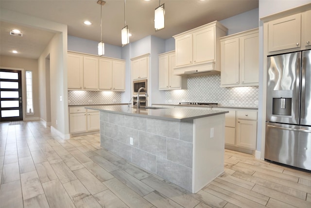 kitchen featuring range hood, wood finish floors, backsplash, appliances with stainless steel finishes, and an island with sink