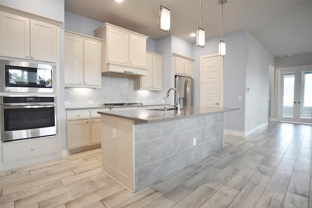 kitchen featuring decorative backsplash, an island with sink, stainless steel appliances, under cabinet range hood, and a sink