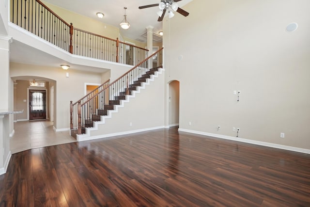 unfurnished living room featuring arched walkways, dark wood-style flooring, stairway, a high ceiling, and baseboards