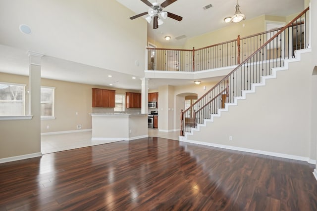 unfurnished living room featuring ceiling fan, wood finished floors, visible vents, baseboards, and stairs