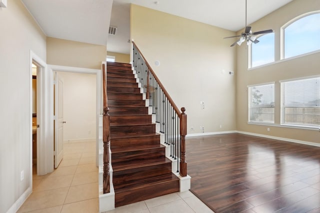 stairs featuring visible vents, a towering ceiling, a ceiling fan, wood finished floors, and baseboards