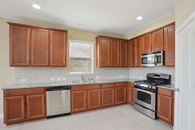 kitchen featuring light stone counters, brown cabinets, stainless steel appliances, tasteful backsplash, and a sink