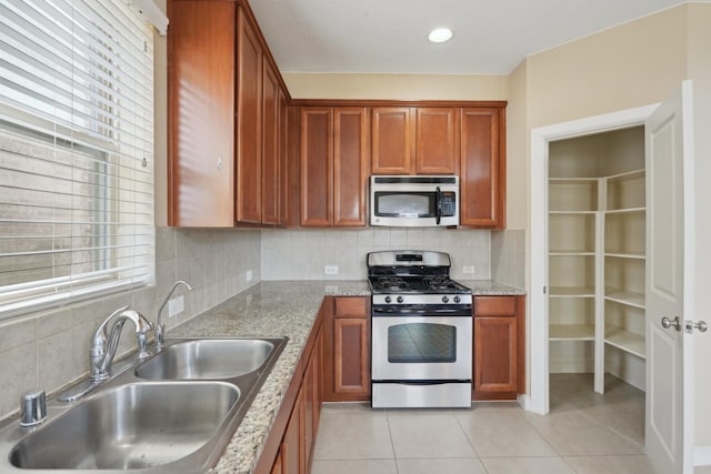 kitchen featuring light tile patterned floors, stainless steel appliances, a sink, backsplash, and brown cabinets