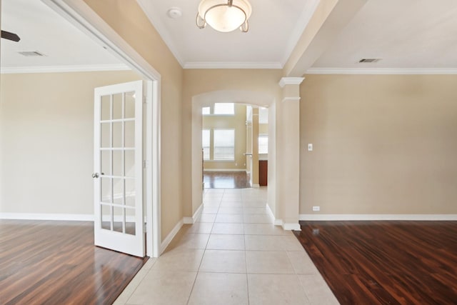 hallway featuring arched walkways, ornamental molding, visible vents, and baseboards