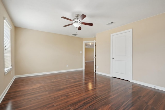 spare room featuring a ceiling fan, visible vents, dark wood finished floors, and baseboards