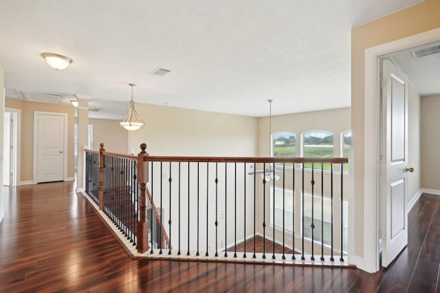 corridor featuring dark wood-style flooring, an upstairs landing, visible vents, and baseboards