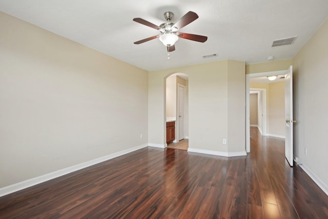 empty room featuring arched walkways, dark wood-style flooring, visible vents, and baseboards