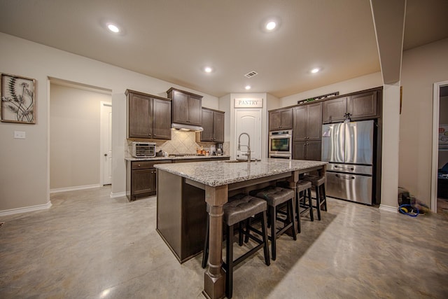 kitchen with appliances with stainless steel finishes, sink, backsplash, a kitchen breakfast bar, and a kitchen island with sink