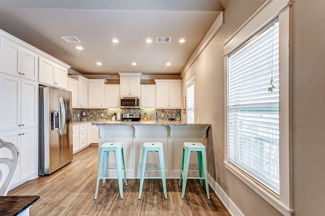 kitchen featuring a kitchen bar, white cabinetry, tasteful backsplash, stainless steel appliances, and light stone countertops