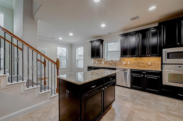 kitchen featuring backsplash, ornamental molding, a center island, light stone counters, and stainless steel appliances