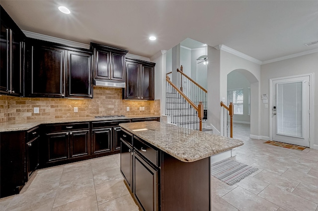 kitchen featuring decorative backsplash, stainless steel gas stovetop, a center island, and dark brown cabinets