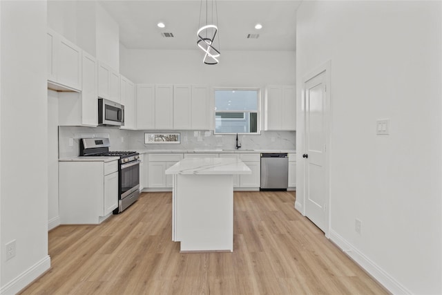 kitchen with appliances with stainless steel finishes, sink, white cabinets, hanging light fixtures, and a center island