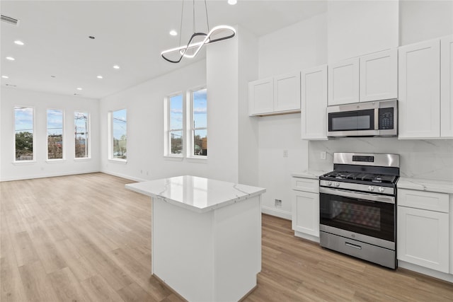 kitchen featuring hanging light fixtures, a kitchen island, stainless steel appliances, light stone countertops, and white cabinets