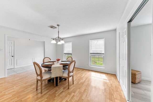 dining room featuring crown molding, a chandelier, a textured ceiling, and light wood-type flooring