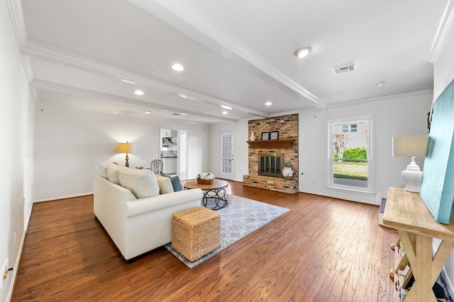 living room featuring a brick fireplace, beam ceiling, ornamental molding, and hardwood / wood-style flooring