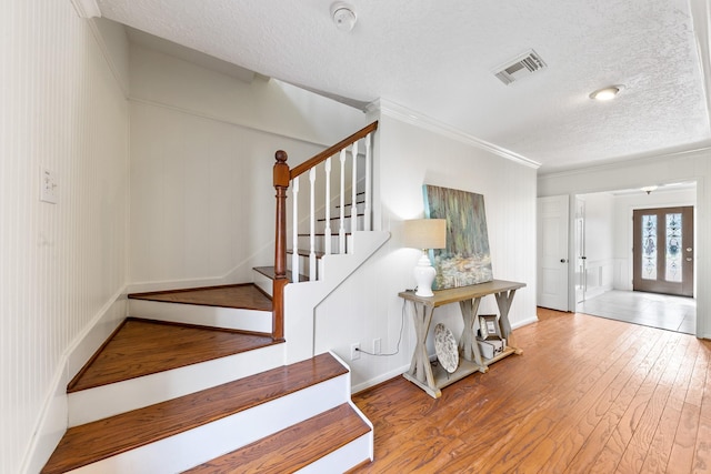 stairs featuring hardwood / wood-style flooring, ornamental molding, a textured ceiling, and french doors