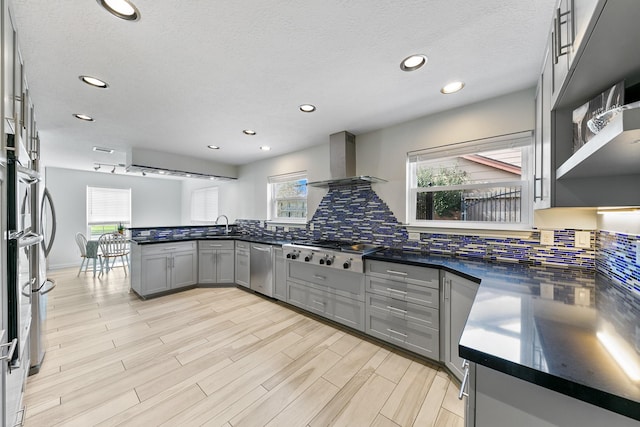 kitchen featuring wall chimney exhaust hood, gray cabinetry, stainless steel appliances, light hardwood / wood-style floors, and backsplash