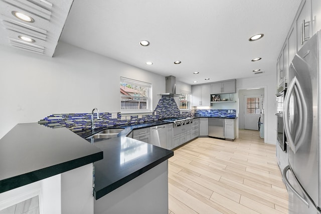 kitchen featuring sink, gray cabinetry, appliances with stainless steel finishes, kitchen peninsula, and wall chimney range hood