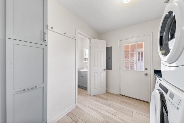 washroom featuring stacked washer and dryer, sink, cabinets, light hardwood / wood-style floors, and a textured ceiling