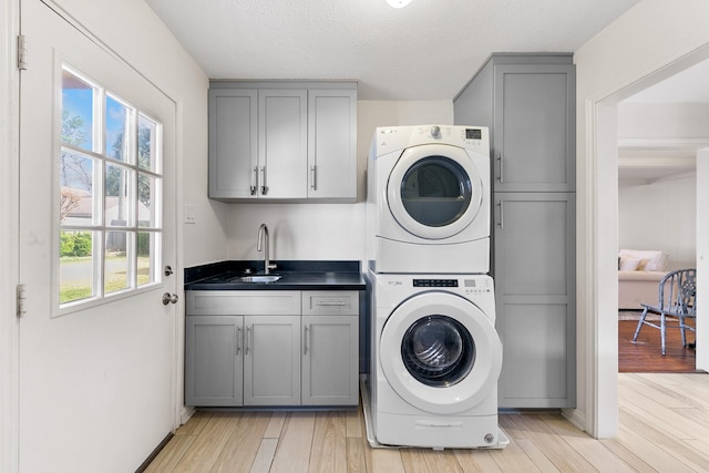 laundry room with sink, light hardwood / wood-style floors, cabinets, and stacked washer / dryer