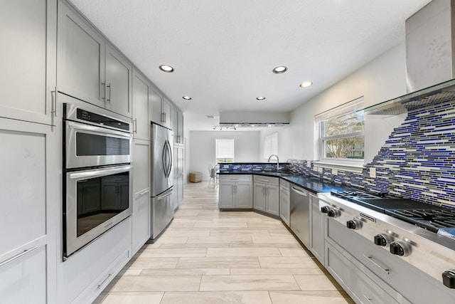 kitchen with sink, gray cabinetry, tasteful backsplash, appliances with stainless steel finishes, and wall chimney range hood