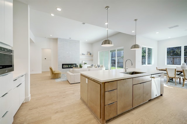 kitchen featuring sink, decorative light fixtures, light wood-type flooring, an island with sink, and oven