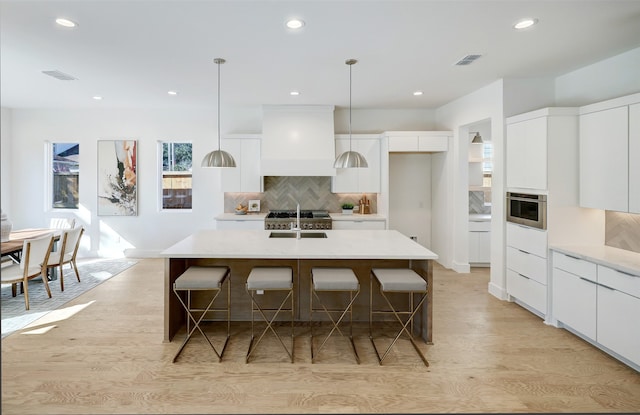 kitchen featuring custom exhaust hood, an island with sink, white cabinetry, and decorative light fixtures