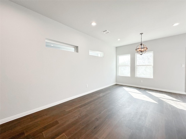 empty room with dark wood-type flooring and an inviting chandelier