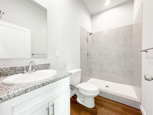 bathroom with wood-type flooring, a tile shower, vanity, and toilet