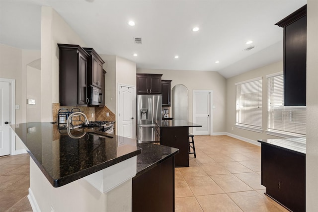 kitchen with stainless steel fridge, a kitchen breakfast bar, dark stone counters, a center island, and light tile patterned floors