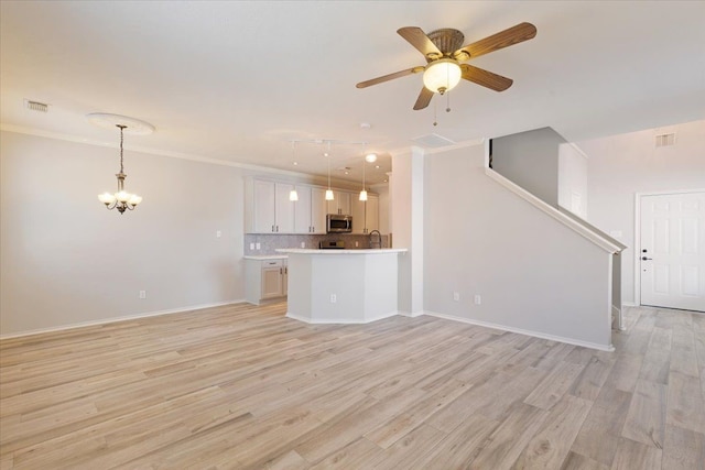 unfurnished living room featuring crown molding, ceiling fan with notable chandelier, and light wood-type flooring