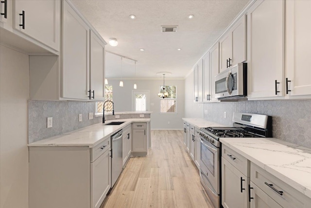 kitchen featuring sink, white cabinetry, hanging light fixtures, appliances with stainless steel finishes, and light stone countertops