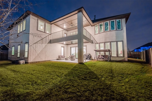 back house at twilight featuring ceiling fan, a balcony, a yard, and a patio