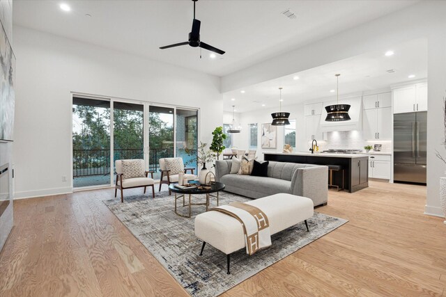 living room with ceiling fan, sink, and light wood-type flooring