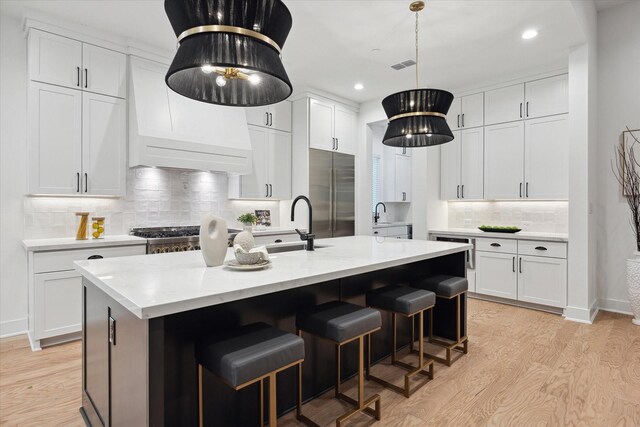 kitchen with white cabinetry, stainless steel built in fridge, and a kitchen island with sink