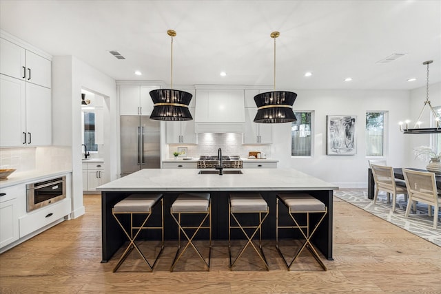 kitchen featuring visible vents, high end refrigerator, light wood-style flooring, white cabinets, and a sink