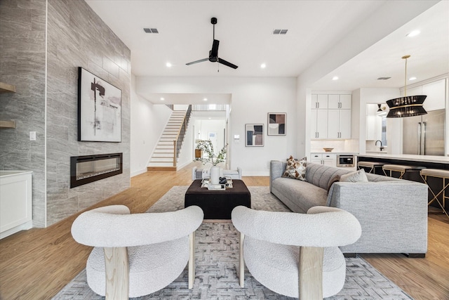 living area with visible vents, light wood-style flooring, stairs, and a tile fireplace