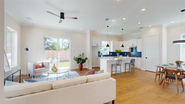 living room with crown molding, ceiling fan, and light wood-type flooring