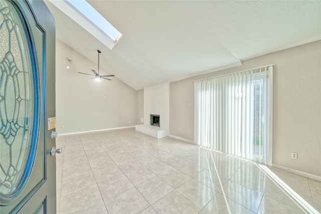 unfurnished living room featuring light tile patterned flooring, a textured ceiling, a large fireplace, ceiling fan, and vaulted ceiling with skylight