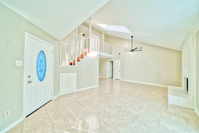 tiled entrance foyer with a textured ceiling, lofted ceiling with skylight, a large fireplace, and ceiling fan