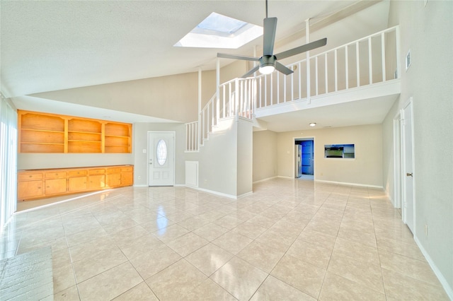 unfurnished living room featuring vaulted ceiling with skylight, light tile patterned floors, a textured ceiling, and ceiling fan