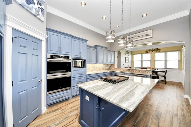 kitchen with a breakfast bar area, ornamental molding, appliances with stainless steel finishes, a kitchen island, and light stone countertops