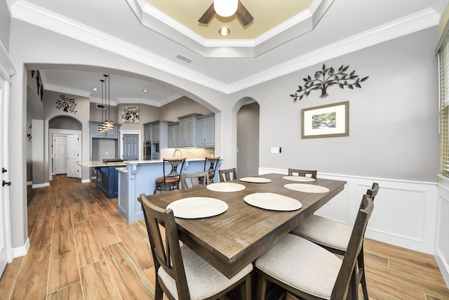 dining area featuring crown molding, a raised ceiling, ceiling fan, and light wood-type flooring