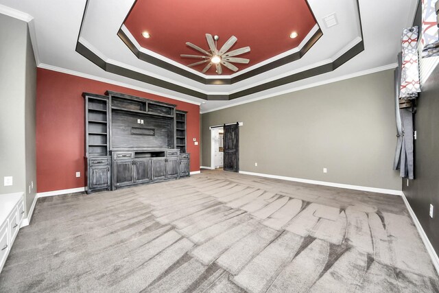 unfurnished living room with a tray ceiling, a barn door, ceiling fan, and carpet flooring