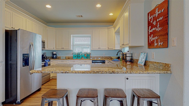 kitchen featuring light stone counters, stainless steel appliances, a peninsula, a breakfast bar, and light wood-type flooring