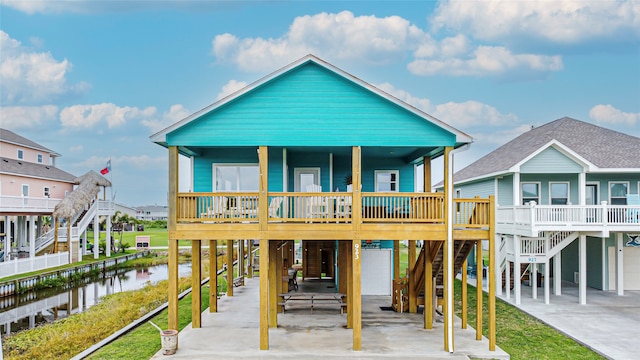 rear view of property with a porch, a water view, stairs, concrete driveway, and a carport