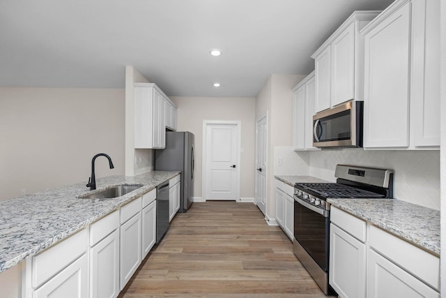 kitchen with white cabinetry, sink, stainless steel appliances, light stone countertops, and light wood-type flooring