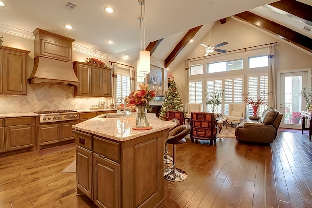 kitchen with stainless steel gas cooktop, tasteful backsplash, hardwood / wood-style flooring, an island with sink, and pendant lighting