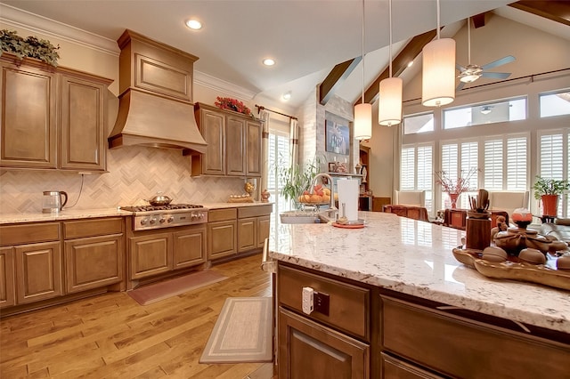 kitchen with light stone countertops, light wood-type flooring, stainless steel gas cooktop, pendant lighting, and a sink